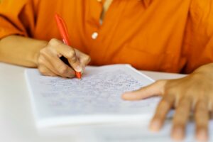 Pessoa escrevendo redação com caneta vermelha, em preparação para o Enem 2025.